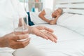 Old elderly woman holding medicine and water on hand on the bed in the bedroom and her husband sleeps beside. Concept of Sleep Royalty Free Stock Photo