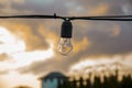 An old electric light bulb hangs on a wire against the background of the evening sky and clouds, close-up, selective focus. Royalty Free Stock Photo