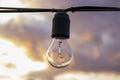 An old electric light bulb hangs on a wire against the background of the evening sky and clouds, close-up, selective focus. Royalty Free Stock Photo