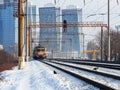 An old electric train moves on rails against the backdrop of a cityscape of skyscrapers on a sunny winter day