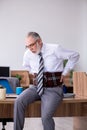 Old male employee suffering from radiculitis at workplace