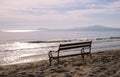 Old empty bench stands on sandy beach and sun reflection on the water Royalty Free Stock Photo