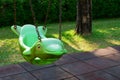 Green hanging swing in dolphin shape and rubber floor tiles with green lawn in outdoor playground area