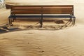 An old empty wooden bench on a sandy beach in the evening against the sunset, seeing a beautiful shadow on the wavy sand Royalty Free Stock Photo