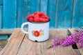 Old enamel cup with handful of fresh rasperries and a bunch violet field flowers on rustic wooden table Royalty Free Stock Photo