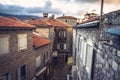 Vintage european city street with orange tile roofs and ancient building facade in front of dramatic sunset sky with antique arch Royalty Free Stock Photo