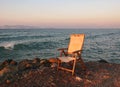 An old fading empty wooden chair in reflected sunset light left next to the sea on a calm summer evening Royalty Free Stock Photo