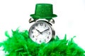 Old fashioned alarm clock wearing a green sparkly hat and boa over white