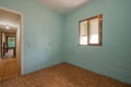 Old fashioned bedroom with small aluminum window, dirty blue painted walls and worn sintasol floors Royalty Free Stock Photo