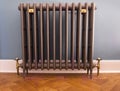 Old fashioned cast iron radiator with brass fittings on herringbone wooden floor