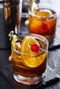 Old fashioned cocktails on cool slate garnished with orange slice, lemon peel, and cherry