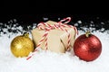 Old fashioned gift wrapped in plain paper, tied with red and white twine sitting in snow beside holiday ornaments Royalty Free Stock Photo