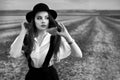 An old-fashioned girl with a suspender and a hat, walking in the field Royalty Free Stock Photo