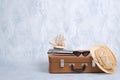 Old fashioned leather travel bag with summer marine accessories: glasses, straw beach hat, toy sailboat on grey background. Banner