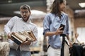 Old-fashioned man carrying heavy pile of books that about to fall from his hands.  female with her cell phone in her hands looking Royalty Free Stock Photo