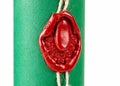 Old fashioned medieval red wax seal imprinted with an ornate design secures a string around a tightly rolled scroll with vibrant