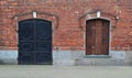 Old fashioned red brick loft wall with a large black metal door and wooden shuttered window Royalty Free Stock Photo