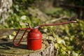 Old fashioned red oil can shot outside on a old tree stump, with green foliage in the background Royalty Free Stock Photo