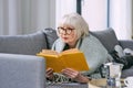 Old fashioned senior woman laying on the couch reading a book. Royalty Free Stock Photo