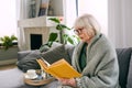 Old fashioned senior woman sitting on the couch reading a book at home. Royalty Free Stock Photo