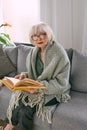 Old fashioned senior woman sitting on the couch reading a book at home. Royalty Free Stock Photo