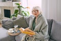 Old fashioned senior woman sitting on the couch reading a book at home. Royalty Free Stock Photo