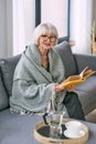 Old fashioned senior woman sitting on the couch reading a book at home. Royalty Free Stock Photo