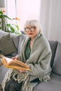 Old fashioned senior woman sitting on the couch reading a book at home. Royalty Free Stock Photo