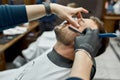 Old fashioned shaving. Barber shaving young handsome bearded man with dangerous straight razor. Working in barbershop