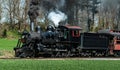 Old-fashioned steam locomotive chugs along a set of railroad tracks, emitting a plume of steam.