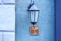 Old-fashioned street wall lamp made of black metal on blue wall facade of an old building with column and informational Royalty Free Stock Photo