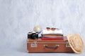 Old fashioned travel suitcase with summer accessories: glasses, pack of clothing, retro photo camera, straw beach hat on grey back