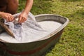 An old fashioned washing trougth filled with water, a vintage washboard, hands and soap that wash the laundry