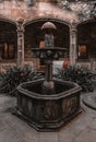 Old-fashioned water fountain with flowerpots in a stone-paved outdoor courtyard Royalty Free Stock Photo