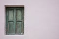 Old fashioned worn window with green wooden shutters, closed, on painted wall background