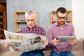 Old father reading newspaper and his son using tablet Royalty Free Stock Photo