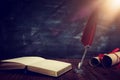 Old feather quill ink pen with inkwell and old books over wooden desk in front of black wall background. Conceptual photo on Royalty Free Stock Photo