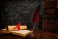 Old feather quill ink pen with inkwell and old books over wooden desk in front of black wall background. Conceptual photo on Royalty Free Stock Photo