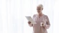 Old female author reading manuscript and drinking tea