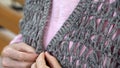 Old female hands buttoning up knitted cardigan, handmade, retirement hobby