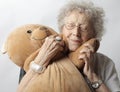 Old female hugging a toy bear against a white wall Royalty Free Stock Photo