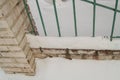 Old fence with metal bars and brick posts, cracked plaster due to adverse weather conditions, outdoors, snow, winter, cold