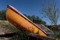 Old fibreglass yellow boat, possibly canoe, drawn ashore in river dam yacht club and tied with chain.