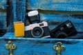 Old film camera with flash, film case and old mirorless black camera on a blue wooden background.