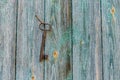 An old forged beautiful rusty key hangs on an old iron nail on a wooden wall, with peeling paint