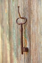 An old forged beautiful rusty key hangs on an old iron nail on a wooden wall, with peeling paint