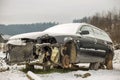 Old forsaken abandoned rusty broken trash car covered with snow without wheels on winter day outdoors in field