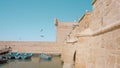 Old fortress and the calm sea with flying seagulls and moored boats. Action. Castle on a blue sky background.