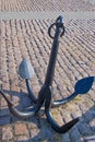 Old four legged anchor with almond shaped points at ends painted black with  ring at top standing on a paved square Royalty Free Stock Photo