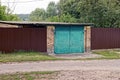 Old garage with green gate and brown metal fence on the street in the grass Royalty Free Stock Photo